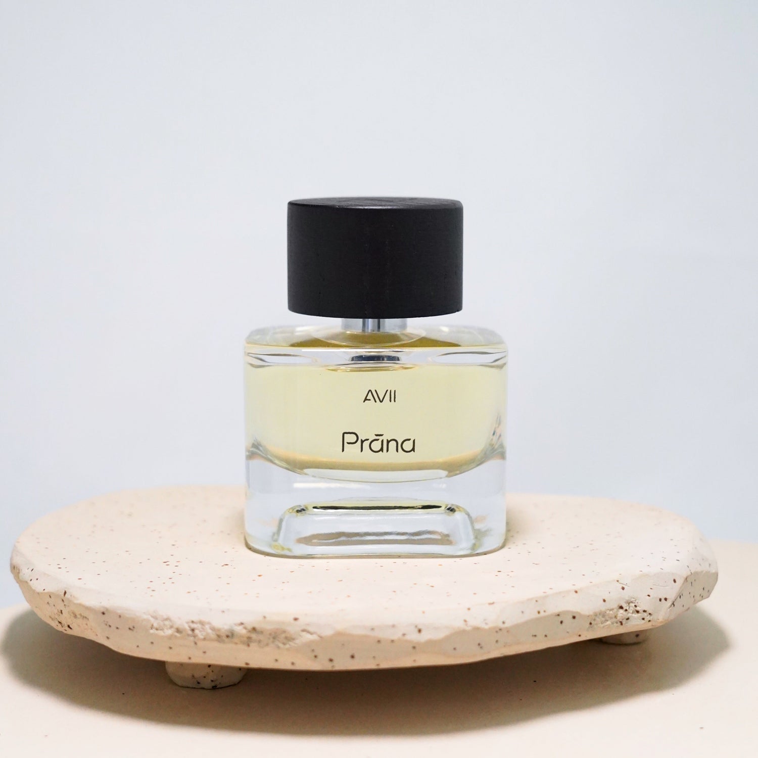 Perfume bottle labeled 'Prána' on a stone surface with a light gray background